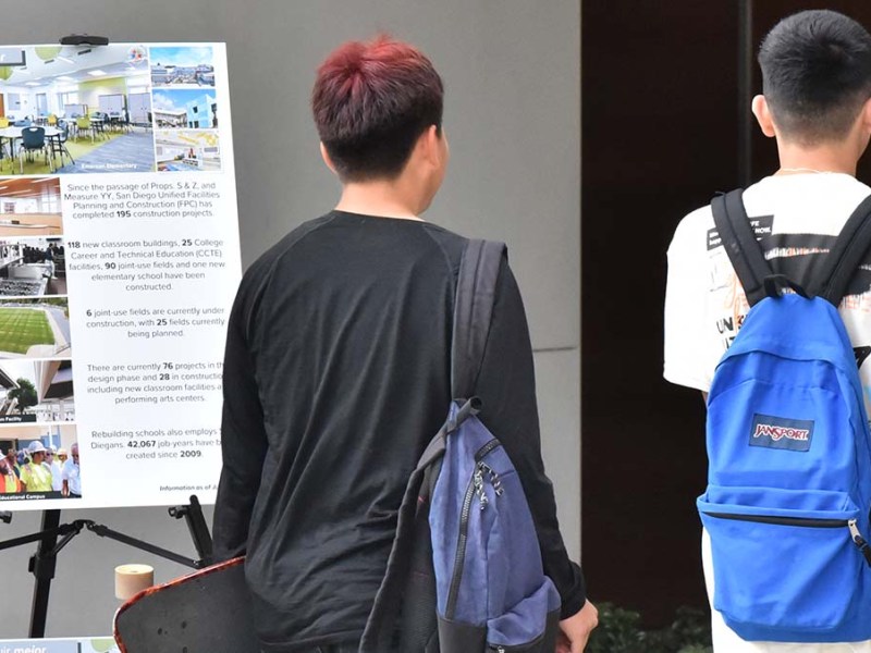 High school students walk past a board illustrating their new school. Photo by Chris Stone