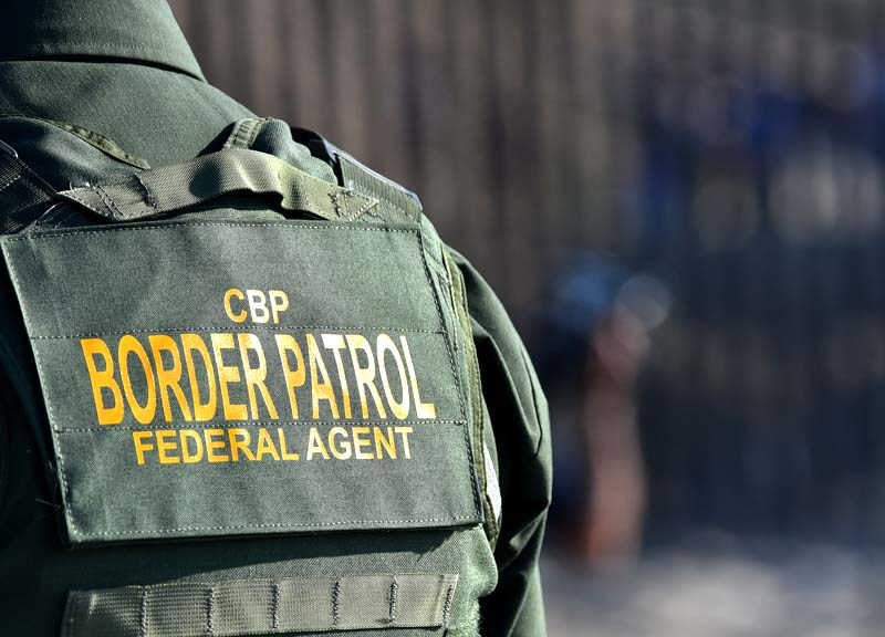 A Border Patrol agent is positioned by the border fence.