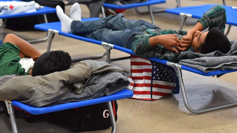 Two young men seeking asylum rest on cots while waiting to begin their journey to their sponsors.