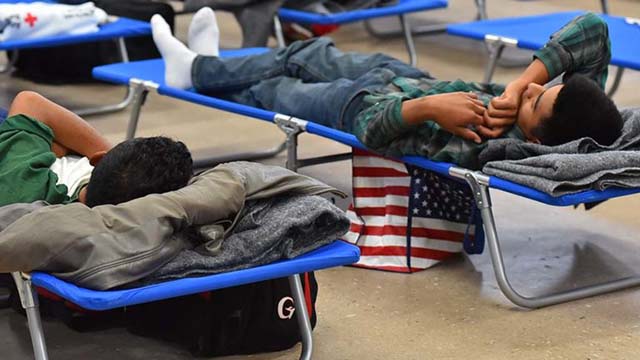 Two young men seeking asylum rest on cots at a former shelter while waiting to begin their journey to their sponsors.