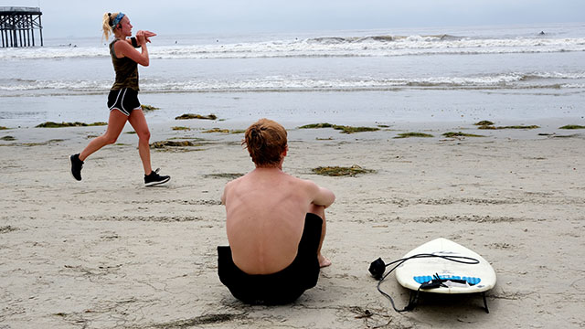 A surfer takes a momentary rest as a jogger stays on pace at Pacific Beach.