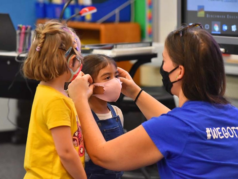 A teacher adjusts a mask on one of her students at Lafayette Elementary School in Clairemont on the first day back to school.