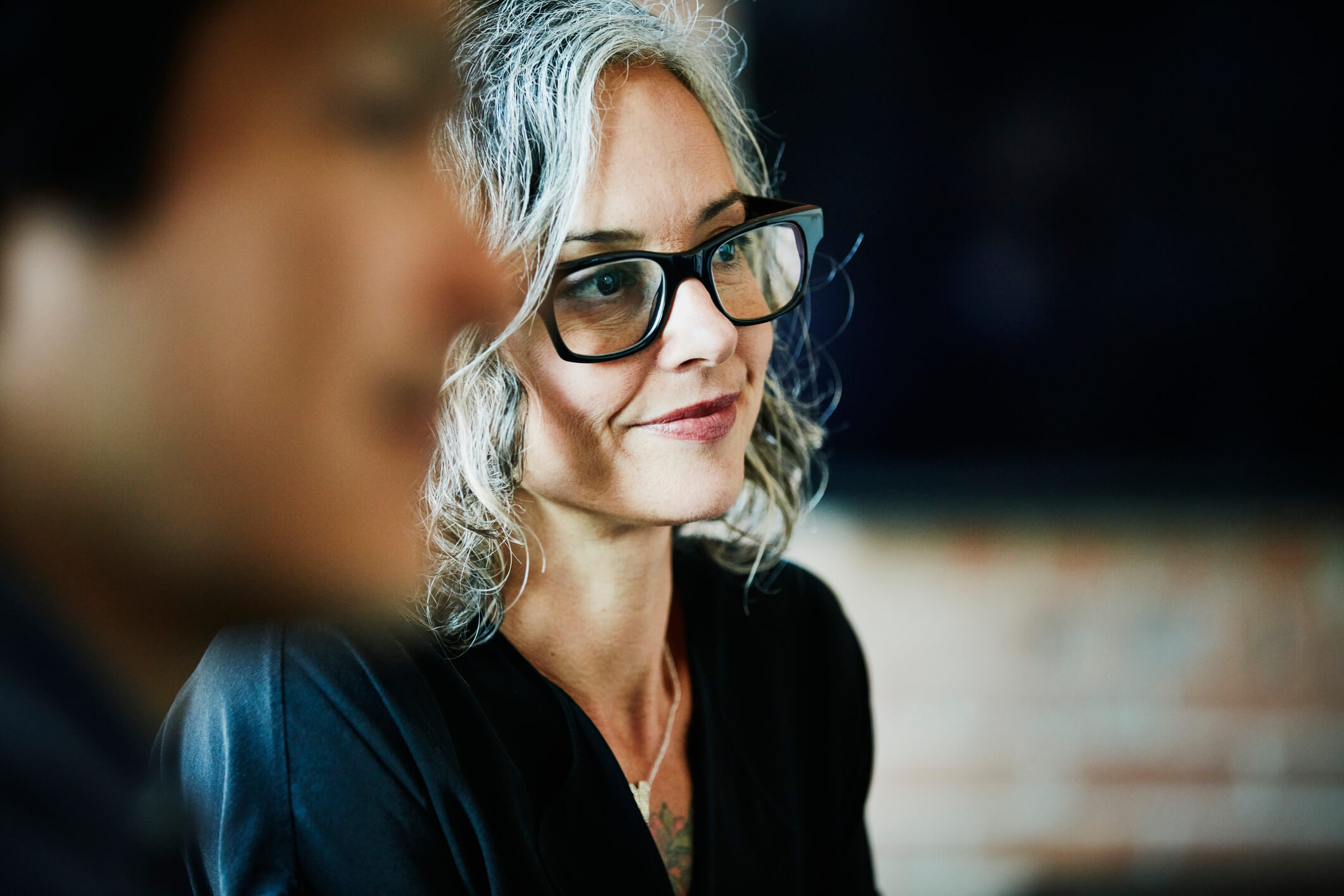 woman with grey hair and black glasses smiling in a meeting