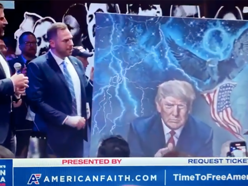 Eric Trump accepts a local artist's painting of his father with two eldest sons and a Q in corner.